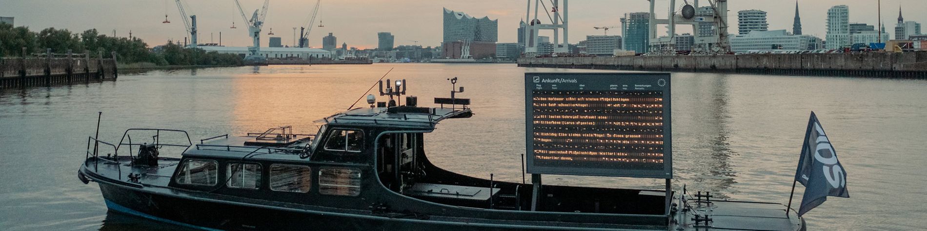 Schute des Kunstprojekts FIDS Open Research Lab im Hamburger Hafen mit elektronischer Anzeigetafel für Vogelflugrouten